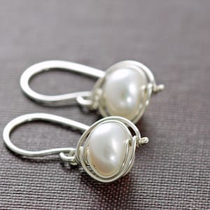 May include: A pair of silver wire wrapped earrings with white pearl accents.