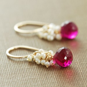 May include: A pair of gold earrings with a pink gemstone and a cluster of white pearls hanging from each earring.