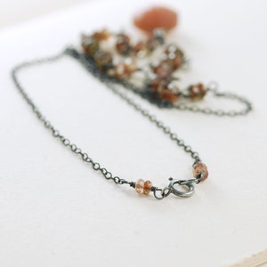 May include: A delicate silver chain necklace with small brown gemstone beads. The necklace has a lobster clasp closure.