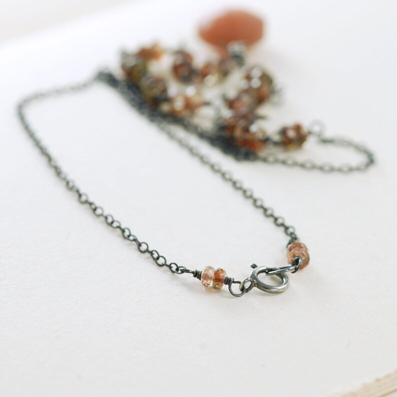 May include: A delicate silver chain necklace with small brown gemstone beads. The necklace has a lobster clasp closure.