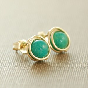 May include: A pair of gold-toned earrings with green gemstone cabochons. The earrings are made with wire wrapped around the stones.