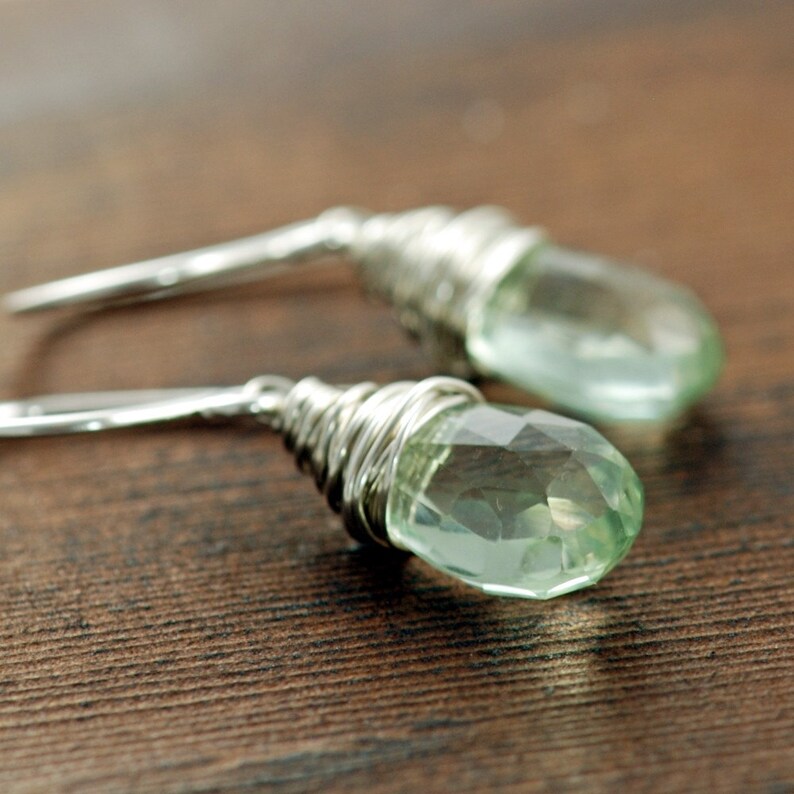 Puede incluir: Un par de pendientes de plata con gotas de piedras preciosas verde claro envueltas en alambre de plata.