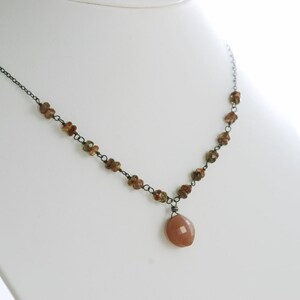 May include: A delicate necklace with a brown gemstone pendant. The necklace is made of black wire and features small brown gemstones.