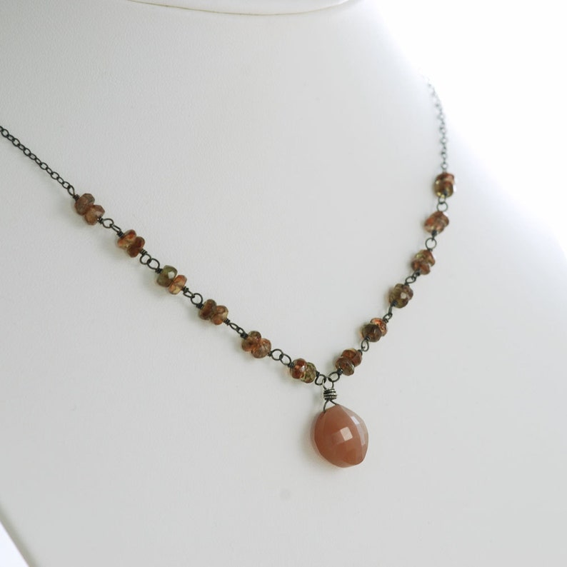 May include: A delicate necklace with a brown gemstone pendant. The necklace is made of black wire and features small brown gemstones.