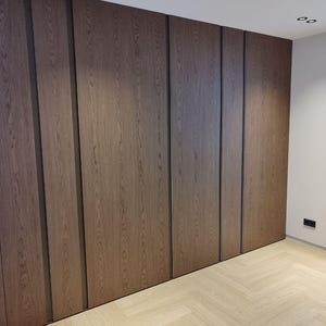 Puede incluir: Una pared con un diseño de paneles de madera. Los paneles son de madera marrón oscura con un ribete de madera marrón claro. El suelo es de madera clara con un patrón de espiga.
