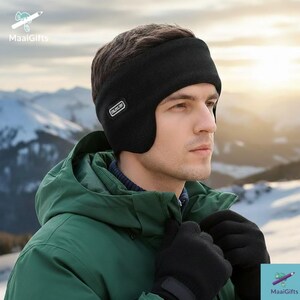 Pu&ograve; includere: Un paraorecchie nero con un piccolo logo bianco sul lato. La persona indossa una giacca verde e guanti neri. Lo sfondo mostra una catena montuosa innevata.