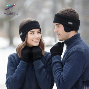 Pu&ograve; includere: Una coppia indossa paraorecchie e guanti in pile neri abbinati. I paraorecchie hanno un piccolo logo rettangolare sul lato. Entrambi indossano maglioni a collo alto blu navy. Lo sfondo &egrave; sfocato.