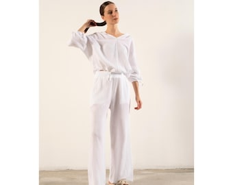 May include: A white, loose-fitting, long-sleeved top with a V-neck and a white pair of wide-leg pants. The pants have a drawstring waist.