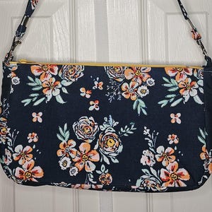 Cartera hecha a mano para adulto en color azul con flores blancas, rosas y verdes con correas para el hombro
