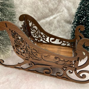 Può includere: Una slitta di legno con intricati disegni ritagliati, perfetta per la decorazione natalizia. La slitta è realizzata in legno marrone scuro e ha un aspetto rustico e vintage.
