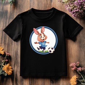 May include: Black t-shirt with a cartoon bunny wearing a blue soccer jersey and kicking a soccer ball. The bunny is in a circle with a blue outline.