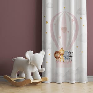 Puede incluir: Un caballo de balancín blanco con una cabeza de elefante gris y un globo aerostático rosa con personajes de animales. El globo tiene un patrón de rayas rosa y blanco con corazones dorados. El fondo es una pared rosa claro.