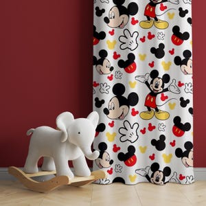 Puede incluir: Cortina blanca con un patrón repetido de Mickey Mouse en rojo, amarillo y negro. La cortina está colgada en una habitación con un juguete de elefante de balancín blanco en primer plano.