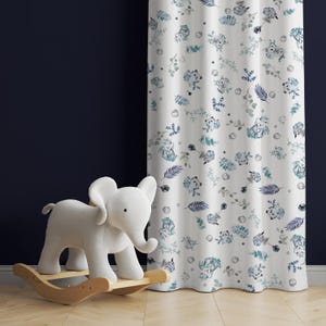 Könnte beinhalten: Weiße Vorhänge mit einem sich wiederholenden Muster aus blauen und grünen Aquarellblättern, Blumen und kleinen Tieren. Ein weißes Schaukelpferd steht im Vordergrund.