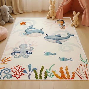 Puede incluir: Una alfombra rectangular para niños con temática submarina. La alfombra presenta ilustraciones de una ballena, un tiburón, un pulpo, un caballito de mar y peces en tonos azules, verdes y naranjas sobre un fondo crema. Corales y algas bordean la alfombra.