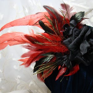 May include: A black velvet hat with a large black fabric rose and red and gold feathers.