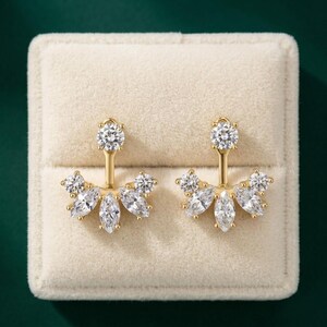 May include: A pair of gold-tone ear jackets featuring a single round-cut clear stone at the top post and a fan-shaped base adorned with a combination of round-cut and marquise-cut clear stones arranged in a symmetrical, multi-faceted design.