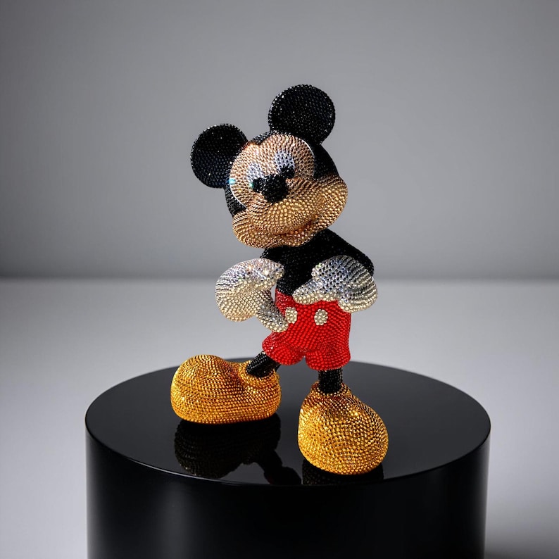Full-length, slightly angled view of the "MICKEY LOVE" Pop Art statue by artist NOISYX. The iconic Mickey Mouse figurine is a signed collectible, meticulously covered in sparkling hand-applied glass rhinestones in black, gold, red, and silver. This handmade bling sculpture rests on a black, cylindrical pedestal, showcasing its unique pop culture design and luxurious aesthetic. Perfect as a one-of-a-kind art piece or a high-end gift for a collector.