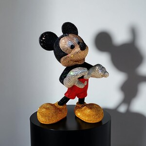 Three-quarter view of the signed "MICKEY LOVE" Pop Art statue by artist NOISYX. This exclusive collectible sculpture features a full body of hand-applied black, gold, and red glass crystals. The image highlights the luxurious bling on Mickey Mouse's face and his iconic red shorts and silver hands. The unique handmade figurine is a statement piece, perfect for collectors seeking high-end pop culture decor or a valuable art gift.