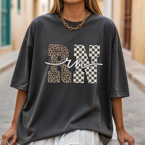 A woman wearing a gray t-shirt with the letters "RN" printed on it, standing on a street.