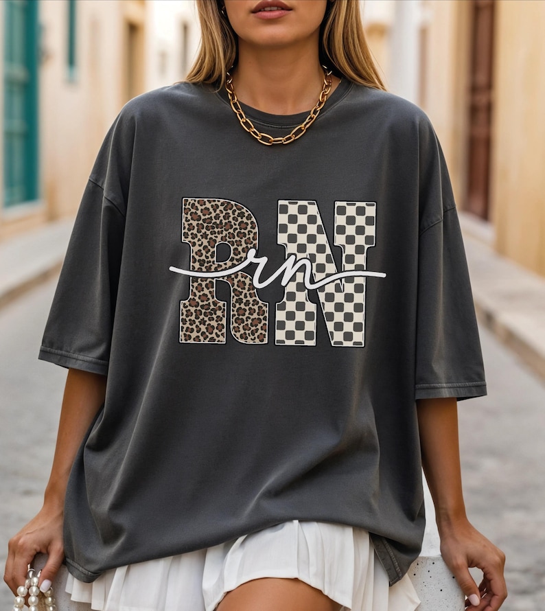 A woman wearing a gray t-shirt with the letters "RN" printed on it, standing on a street.