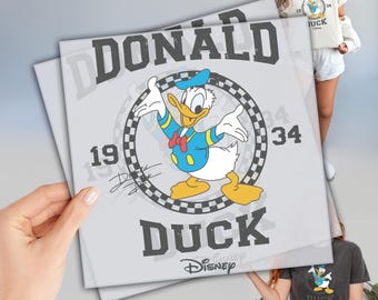 Puede incluir: Una impresión cuadrada gris claro con el Pato Donald en un diseño temático de carreras. La impresión incluye el texto "DONALD DUCK" y "1934" con un logotipo de Disney. El personaje de dibujos animados lleva un traje de marinero azul y un sombrero azul.