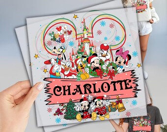 May include: A personalized Christmas-themed print featuring Disney characters like Mickey and Minnie Mouse, Donald Duck, and Goofy. The print includes a castle, snowflakes, and the name "CHARLOTTE" on a pink banner. The design is festive and colorful.