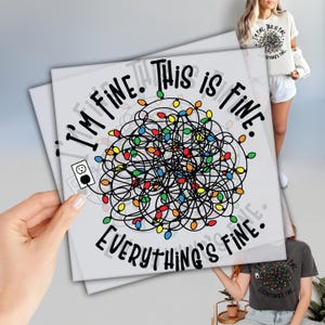 May include: A light gray square print with the text "I'M FINE. THIS IS FINE. EVERYTHING'S FINE." in black. The design features a tangled string of colorful Christmas lights and a plug. The print is held by a person.
