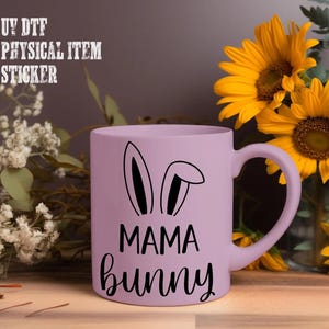 A purple mug with the text "MAMA bunny" printed on it, placed on a wooden surface next to a bouquet of yellow sunflowers.