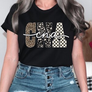 A woman wearing a black t-shirt with the word "CNA" printed on it, along with a patterned design. She is also wearing blue jeans.