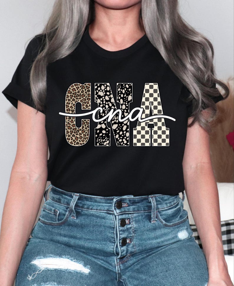 A woman wearing a black t-shirt with the word "CNA" printed on it, along with a patterned design. She is also wearing blue jeans.