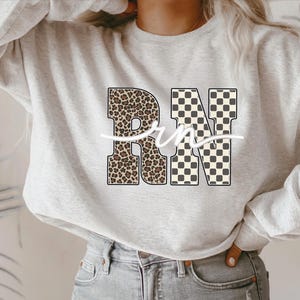 A woman wearing a grey sweatshirt with a leopard print design and the letters "RN" printed on it.