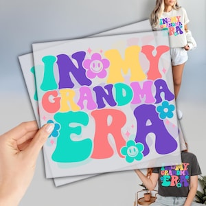 May include: A colorful graphic design with the text "In My Grandma Era" in a retro font. The design features flowers, stars, and smiley faces in pink, blue, yellow, and purple.
