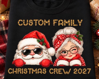 Puede incluir: Una sudadera negra con un gráfico de Santa Claus y la Señora Claus, con el texto "CUSTOM FAMILY" arriba y "CHRISTMAS CREW 2027" abajo. Santa lleva gafas de sol y la Señora Claus lleva gafas con estampado de leopardo y una diadema roja.