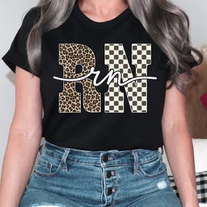 A woman wearing a black t-shirt with the word "RN" printed on it, along with leopard print and checkered designs. She is also wearing blue jeans.