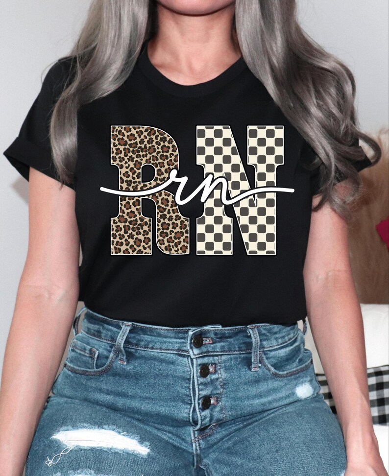 A woman wearing a black t-shirt with the word "RN" printed on it, along with leopard print and checkered designs. She is also wearing blue jeans.