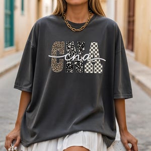 A woman wearing a grey t-shirt with a graphic design and white shorts is walking down a street.