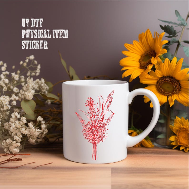A white mug with a red floral design sits on a wooden surface, surrounded by yellow sunflowers and white flowers.