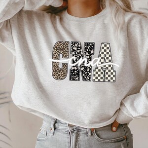 A woman wearing a grey sweatshirt with the letters "CNA" printed on it.