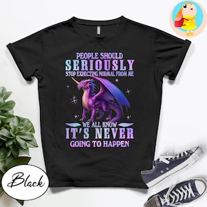 May include: Black t-shirt with a dragon graphic and the text "PEOPLE SHOULD SERIOUSLY STOP EXPECTING NORMAL FROM ME WE ALL KNOW IT'S NEVER GOING TO HAPPEN". The dragon is purple with blue wings.