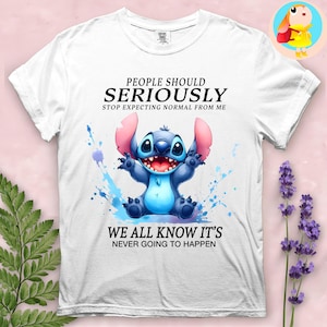 May include: White t-shirt featuring a blue cartoon character with large ears and the text "PEOPLE SHOULD SERIOUSLY STOP EXPECTING NORMAL FROM ME WE ALL KNOW IT'S NEVER GOING TO HAPPEN". The character is surrounded by blue watercolor splashes.