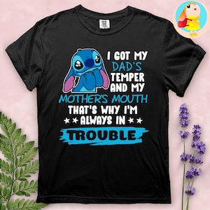 Op de afbeelding: Zwart T-shirt met een blauw stripfiguur en de tekst "I GOT MY DAD'S TEMPER AND MY MOTHER'S MOUTH THAT'S WHY I'M ALWAYS IN TROUBLE". Het ontwerp bevat een blauw figuur met grote ogen en oren.