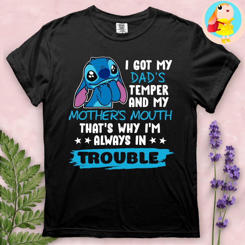 Op de afbeelding: Zwart T-shirt met een blauw stripfiguur en de tekst "I GOT MY DAD'S TEMPER AND MY MOTHER'S MOUTH THAT'S WHY I'M ALWAYS IN TROUBLE". Het ontwerp bevat een blauw figuur met grote ogen en oren.