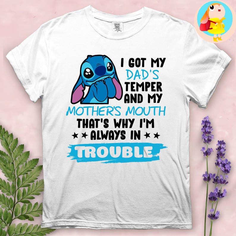 Op de afbeelding: Wit T-shirt met een blauw cartoonfiguur en de tekst "I GOT MY DAD'S TEMPER AND MY MOTHER'S MOUTH THAT'S WHY I'M ALWAYS IN TROUBLE" in zwart en blauw.