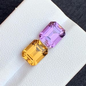 May include: Two faceted gemstones, one is a light purple and the other is a light orange, both are cut in a rectangular shape.