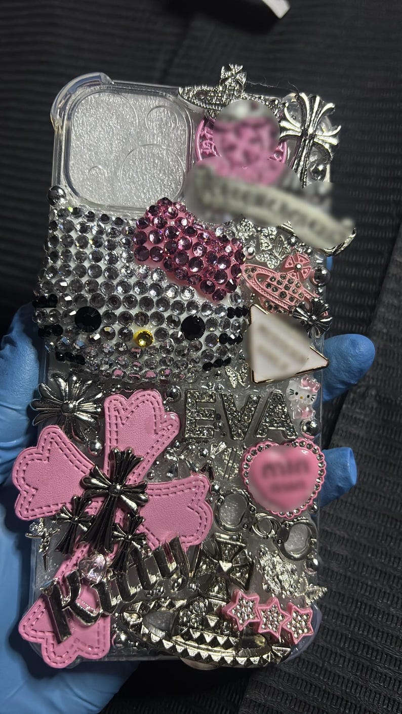 May include: Clear phone case bedazzled with rhinestones, featuring a Hello Kitty design, pink bow, and various silver and pink embellishments. The case includes the name "EVA" and a heart-shaped charm.