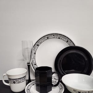 May include: A set of black and white patterned dinnerware, including a mug, a bowl, a plate, a saucer, a glass, and a black mug. The dinnerware features a black floral design on a white background.