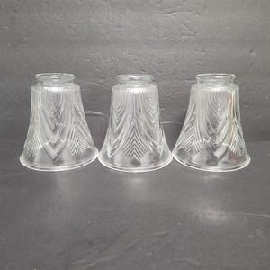 May include: Three clear glass lamp shades with a flared, bell-like shape. Each shade features a vertical, textured pattern that creates a decorative effect. The shades are designed to diffuse light and add a vintage touch to any room.