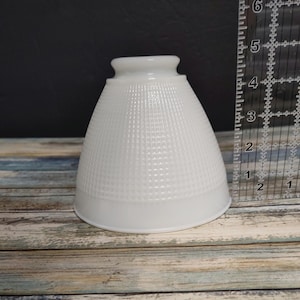 May include: A white, textured glass lampshade with a flared shape. The lampshade has a grid-like pattern and a smooth, rounded top. A ruler is placed next to the lampshade, showing measurements in inches.