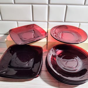 May include: Set of six dark red glass plates, four square and two round, with a raised center. The plates are stacked in two groups, one of four and one of two.